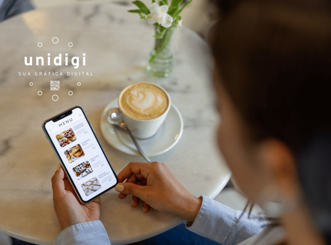pessoas com uma mesa na frente que tem uma xícará de café e está segurando um celular com o cardápio digital nas mãos